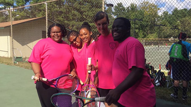 A group of people laughing and posing at a tennis court.