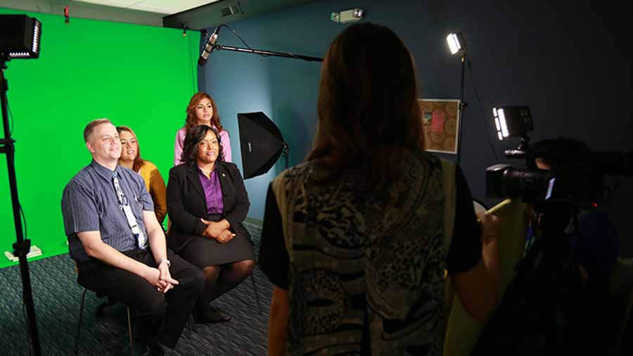 Several people being interviewed in a green screen studio.