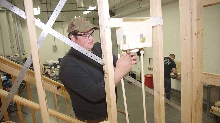 A young plumbing student working in a demo house at school.