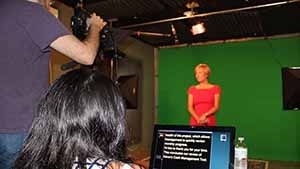 A woman being filmed against in a  green screen studio.